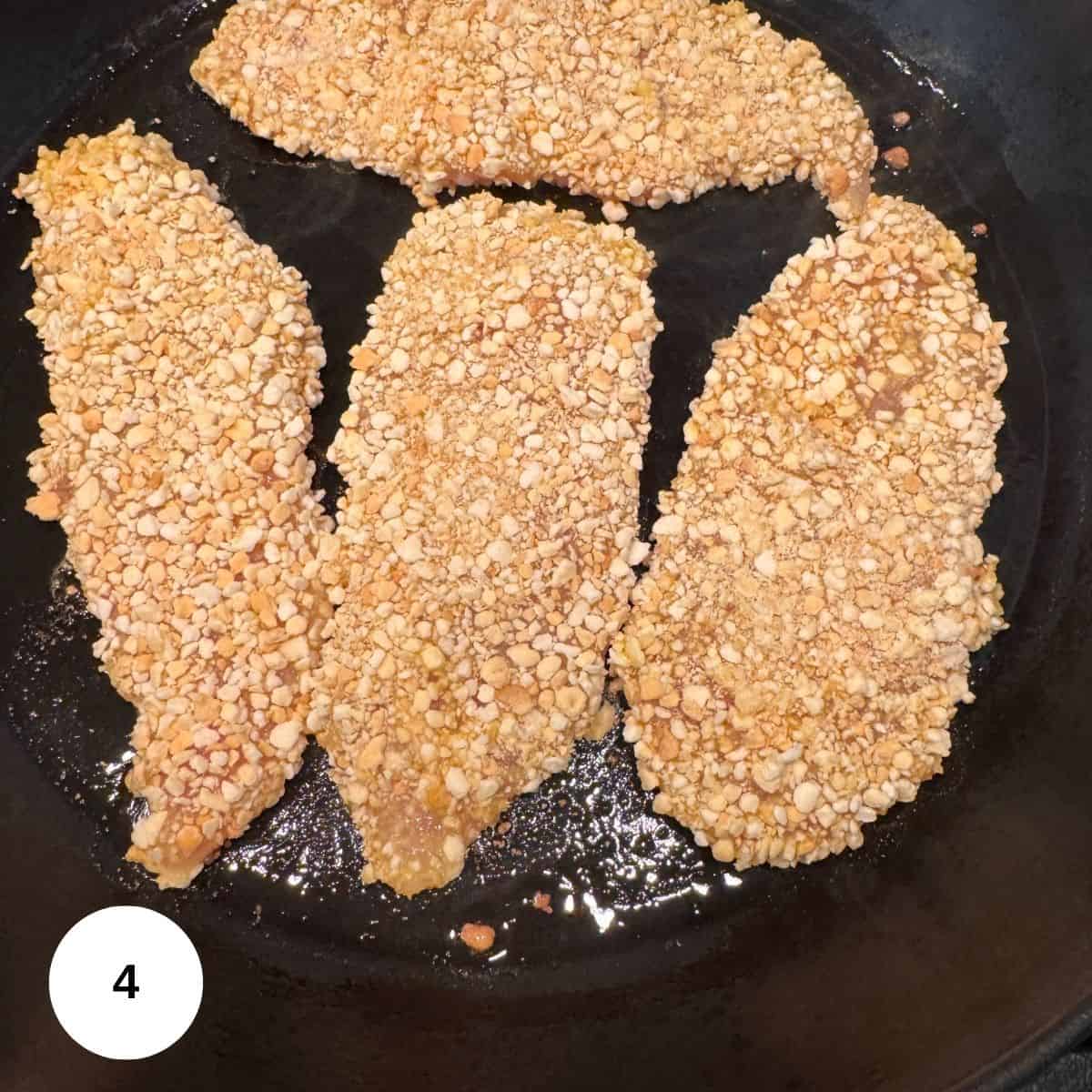 Three gluten-free chicken tenders are cooking in a skillet with some oil. A white circle with the number 4 is in the bottom left corner.