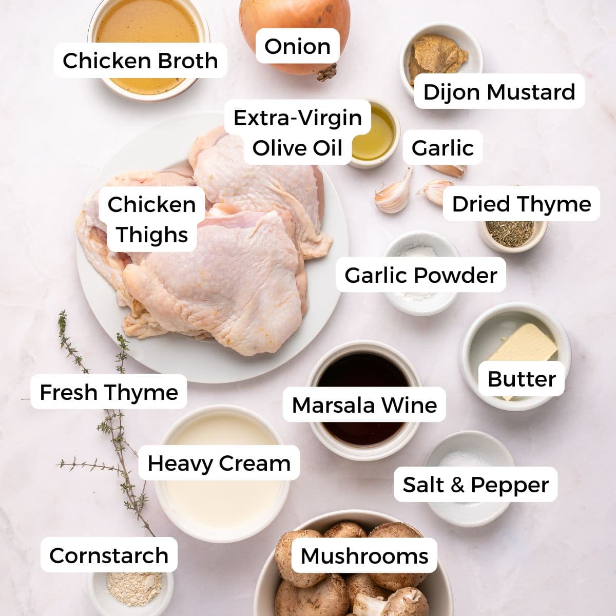 Labeled ingredients for a delicious Chicken Marsala recipe arranged on a white surface, perfect for a one skillet meal. Includes chicken thighs, broth, onion, olive oil, Dijon mustard, garlic, thyme, mushrooms, cream, and more—naturally gluten free.