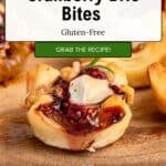 A close-up of a gluten-free cranberry brie bite pastry topped with melty brie cheese and tangy cranberry sauce on a wooden board. Text overlay says Quick & Easy Cranberry Brie Bites, Gluten-Free, Grab the Recipe!.