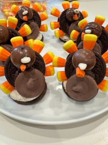 A plate of turkey-shaped Thanksgiving treats from Sunday Thymes, made from chocolate cookies, candy corn, chocolate balls, and frosting, arranged to resemble turkeys with colorful candy tail feathers.