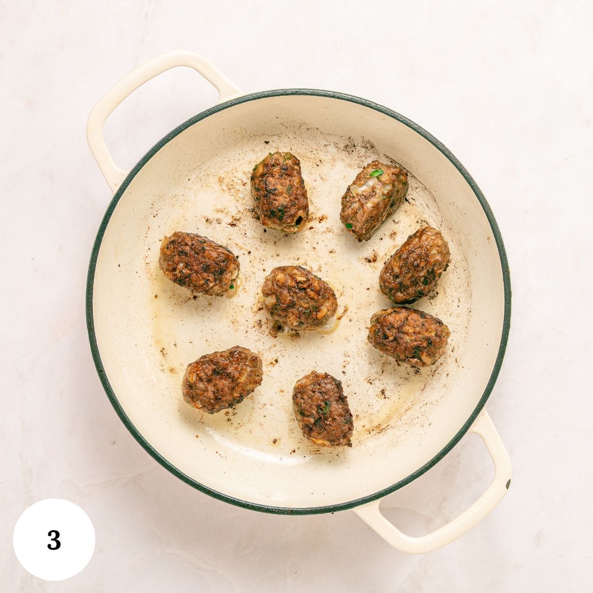 A white pot with eight browned Greek Beef Meatballs arranged in a circle on a light-colored surface. The number 3 is in a white circle in the bottom left corner.