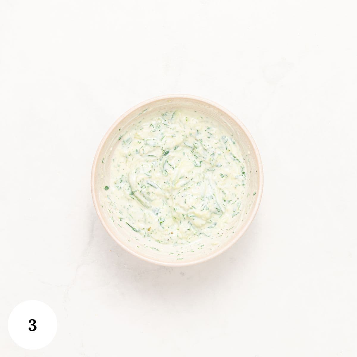 A Mediterranean bowl filled with a creamy, white dip mixed with green herbs sits on a white surface. The number 3 is displayed in a white circle in the bottom left corner.