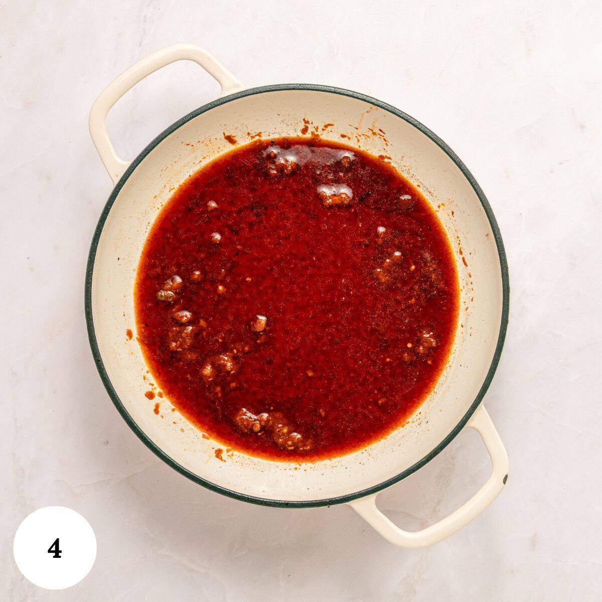 A white pot with handles contains Soutzoukakia-Greek beef meatballs-in a rich, red tomato sauce with small chunks of meat, sitting on a light-colored marble surface. The number 4 appears in a white circle in the bottom left corner.