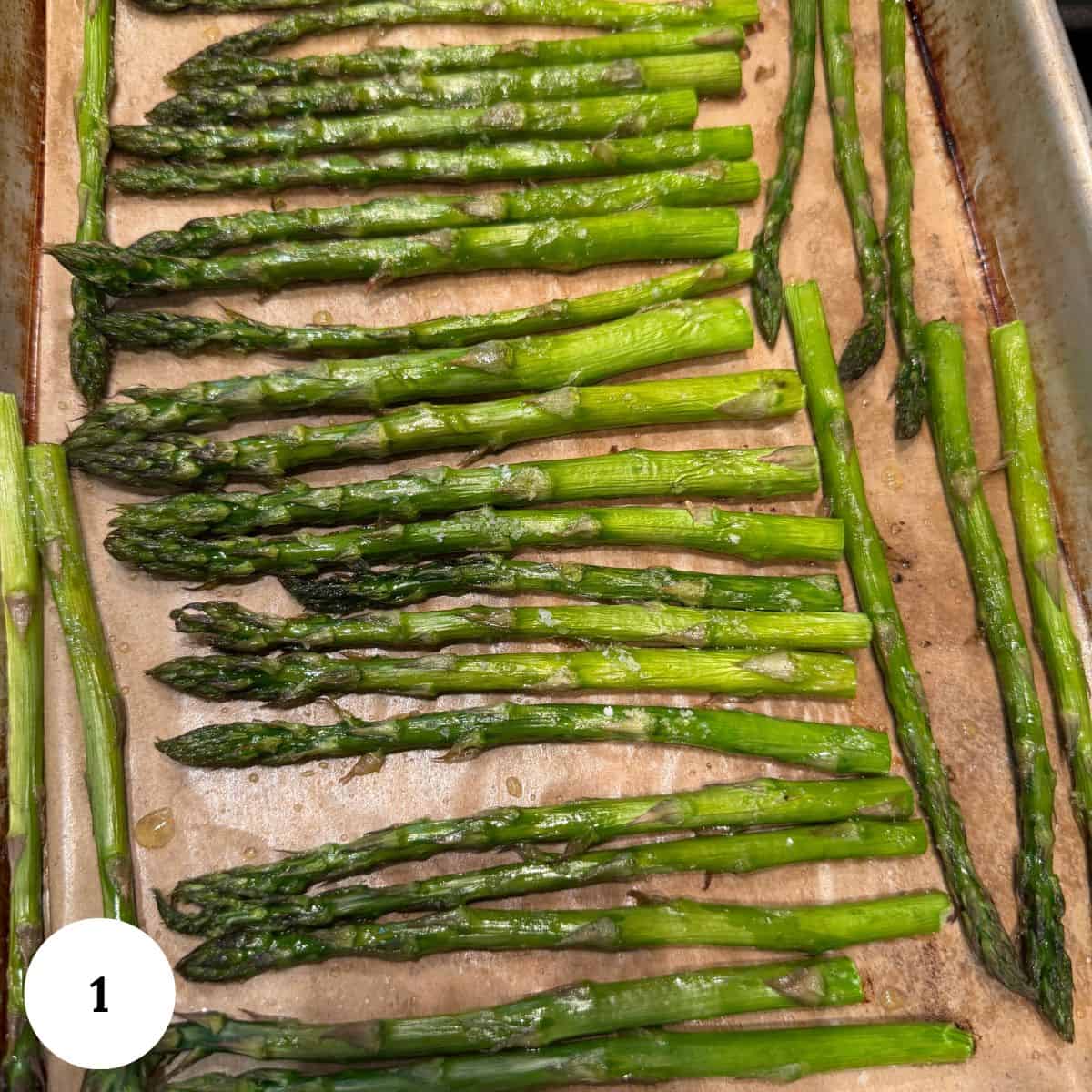 Roasted asparagus with lemon spears arranged in neat rows on a parchment-lined baking sheet, glistening with oil.