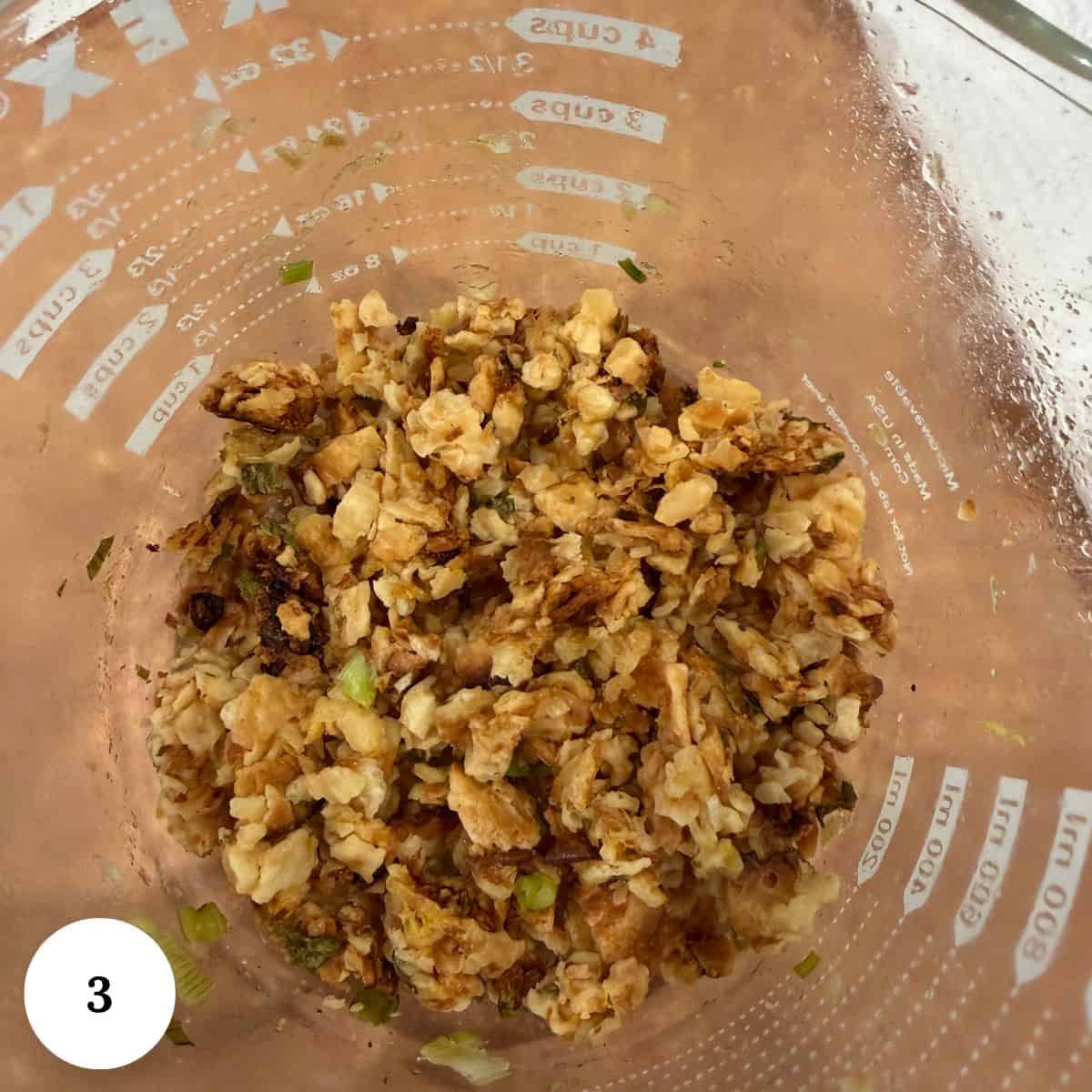 Chopped walnuts mixed with herbs in a clear glass measuring cup, viewed from above-perfect as a topping for roasted asparagus with lemon. The cup features measurement markings and a white circle with the number 3 in the bottom left corner.