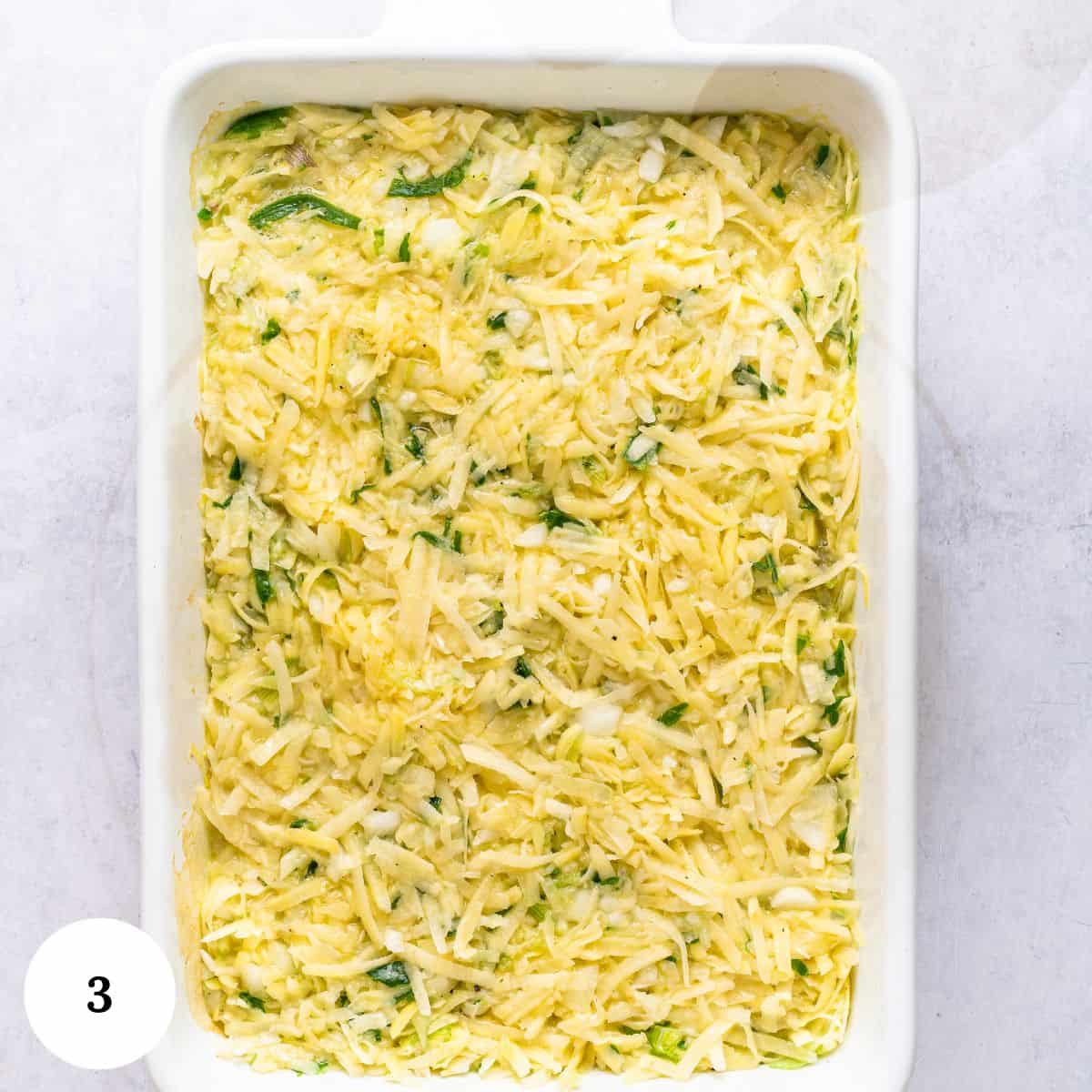 Shredded zucchini and cheese mixture, inspired by classic potato kugel, spread evenly in a white rectangular baking dish, ready to be baked. The photo is labeled with the number 3 in the bottom left corner.