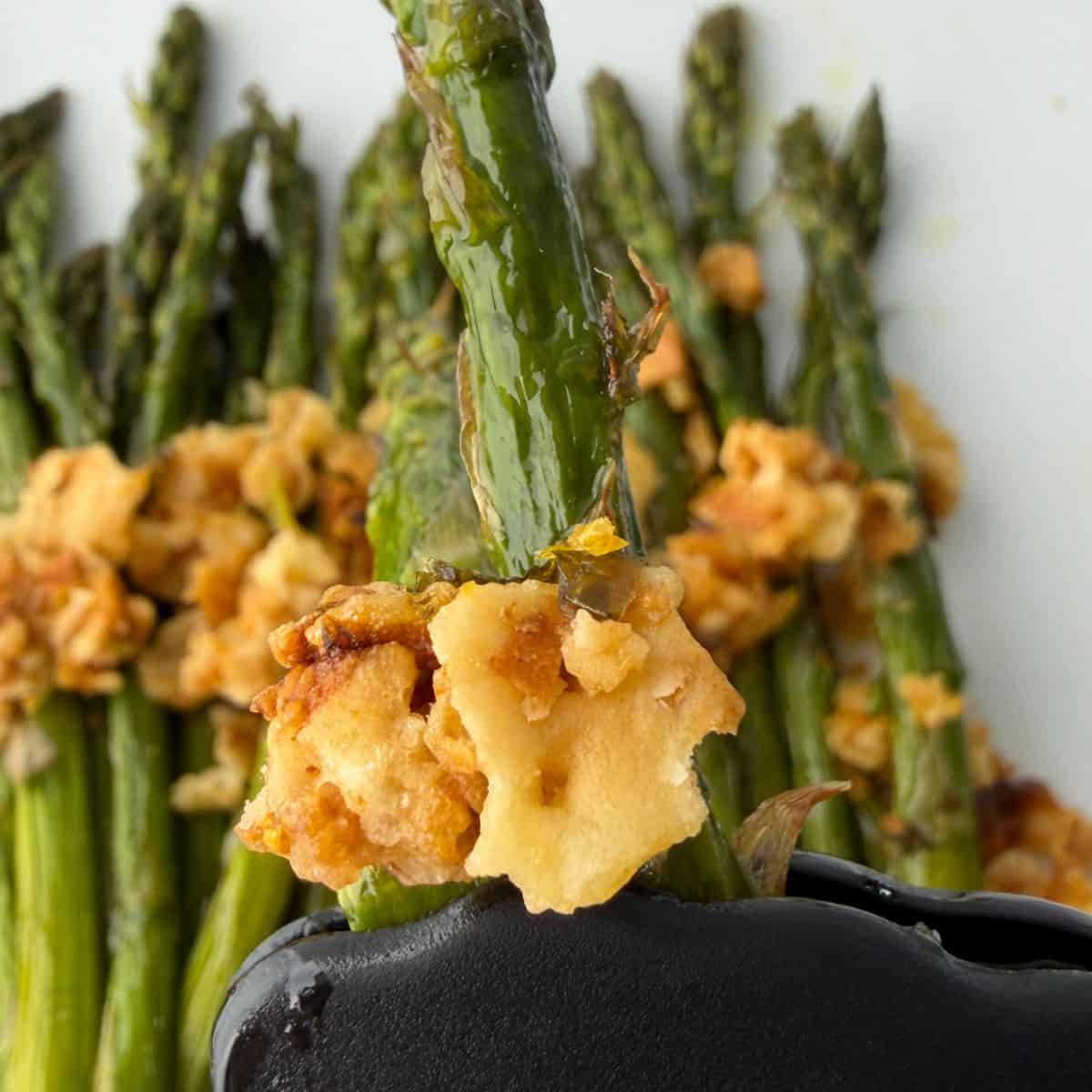 Close-up of roasted asparagus with lemon, topped with a golden, crispy cheese or breadcrumb mixture, served on a white plate.