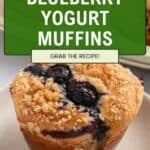 A close-up of blueberry yogurt muffins with crumb topping sits on a plate. Text overlay reads: Bakery-Style Blueberry Yogurt Muffins. Grab the recipe!.
