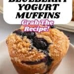A blueberry yogurt muffin with a crumb topping sits on a plate. Text overlay reads: Bakery-Style Blueberry Yogurt Muffins. Try these irresistible blueberry yogurt muffins—grab the recipe!.