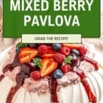 A gluten-free berry pavlova topped with whipped cream, strawberry sauce, strawberries, raspberries, blueberries, and mint. An overlay reads Gluten-Free Mixed Berry Pavlova. Grab the recipe!.
