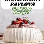 A gluten-free berry pavlova topped with mixed berries and whipped cream sits on a white cake stand. Text overlay reads: Gluten-Free Mixed Berry Pavlova. Grab The Recipe!.