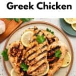 A plate with grilled Greek chicken breasts, garnished with lemon slices and parsley. Text above reads Greek Chicken with Yogurt Marinade. Small bowls with seasonings are nearby.