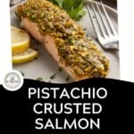A piece of pistachio crusted salmon, garnished with herbs, lemon slices, and parsley, sits on a plate with a fork. Text overlay reads Pistachio Crusted Salmon with Za’atar & Lemon. Download Now.