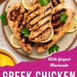 A plate of grilled chicken breasts garnished with lemon slices and parsley, with text overlay that reads Greek Chicken with Yogurt Marinade on a pink background at the bottom.