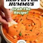 A hand dips a pita chip into a bowl of creamy hummus, garnished with chickpeas and herbs. Text over the image reads “Smoky Hummus with Roasted Red Bell Pepper. Grab the recipe!”.