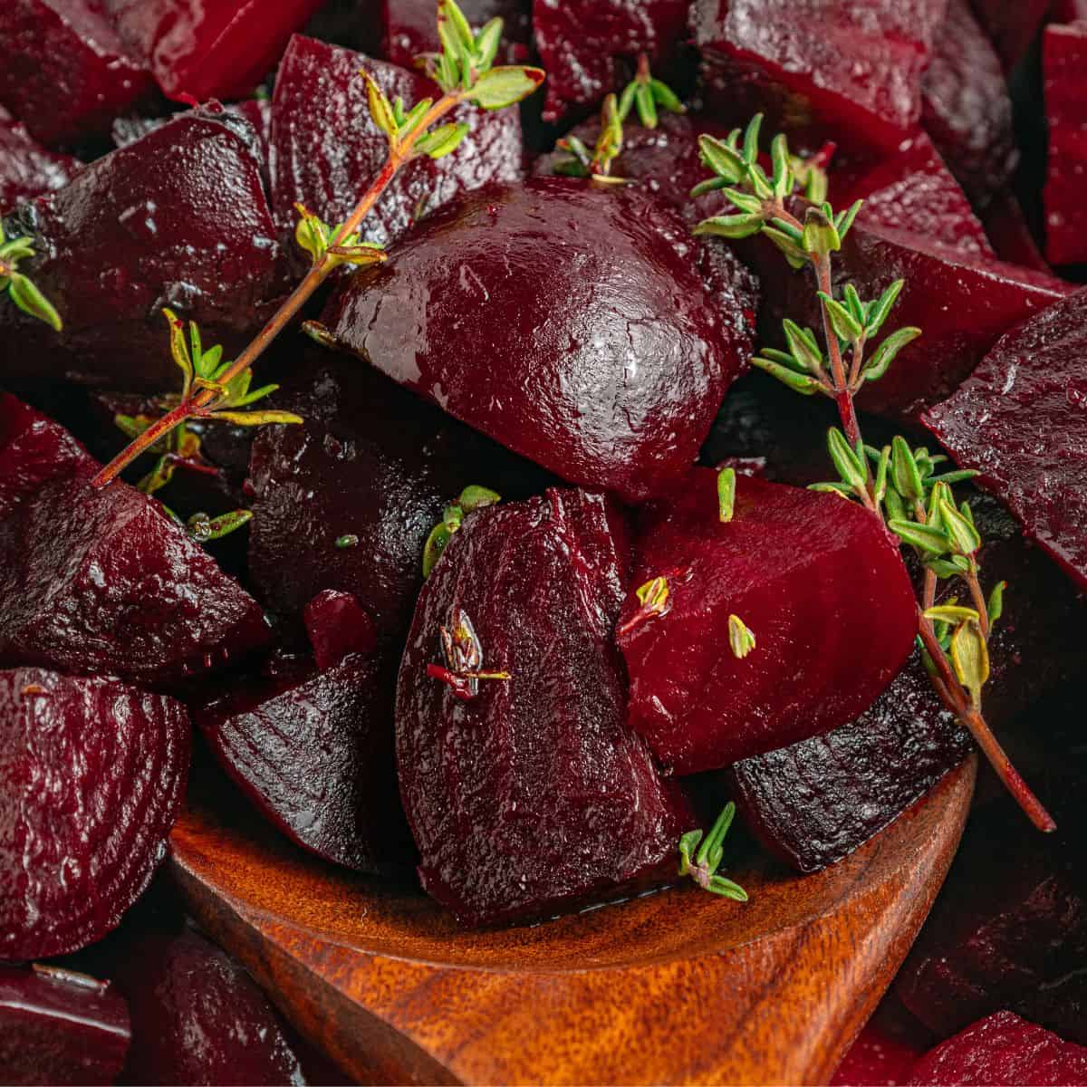 Close-up of roasted beet chunks garnished with fresh thyme sprigs, served in a wooden bowl. The roasted beets have a glossy, deep red color and appear tender and flavorful.