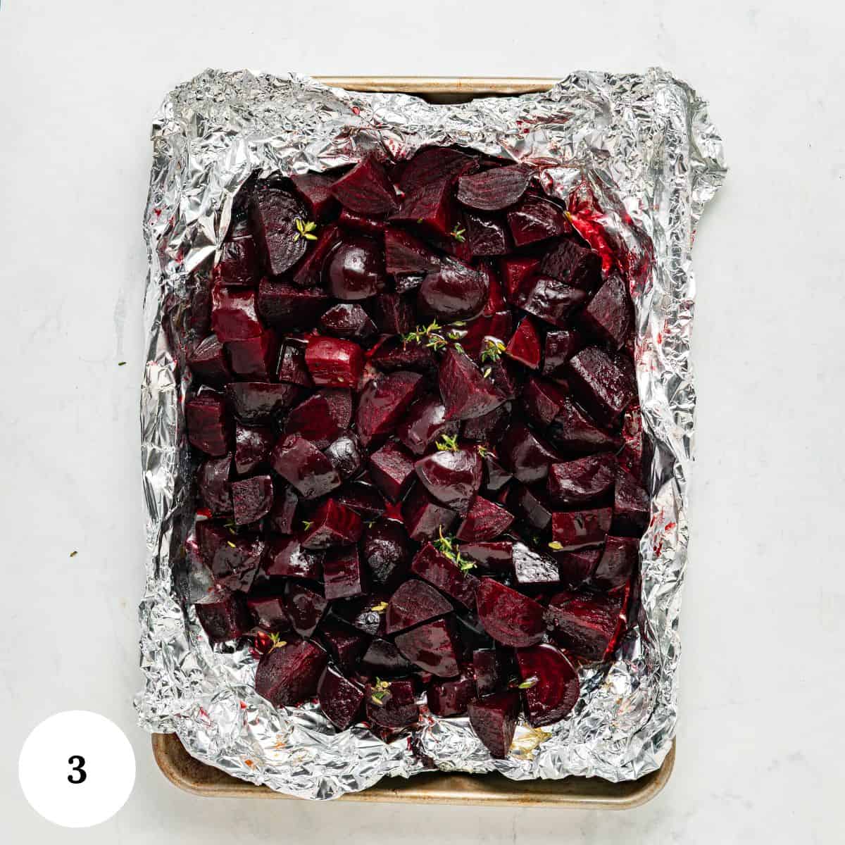 A baking sheet lined with crinkled aluminum foil holds roasted, chopped beets garnished with herbs. The vibrant roasted beets are the focus of the image, which is numbered 3 in a white circle at the bottom left corner.