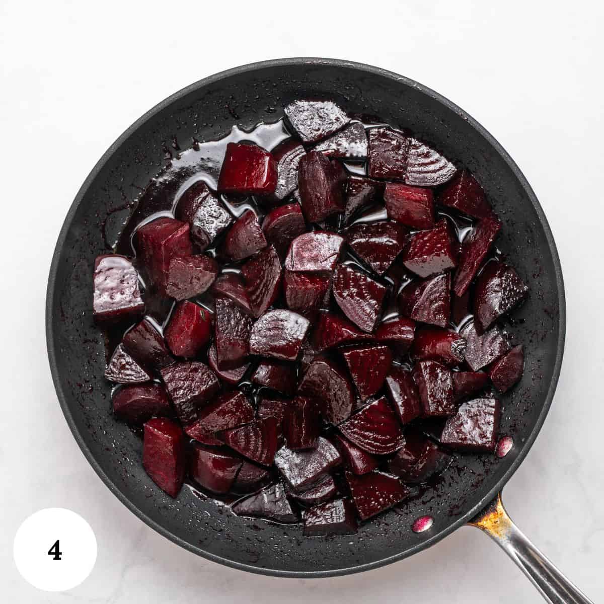 A black skillet filled with cooked, chopped roasted beets in a dark liquid, viewed from above on a white background. A white circle with the number 4 is in the lower left corner.