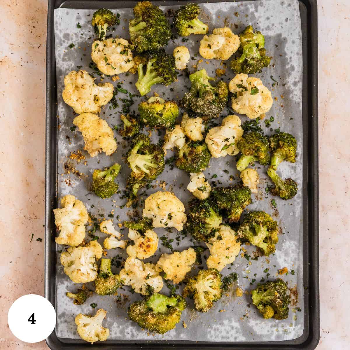 Roasted broccoli and cauliflower florets sprinkled with herbs and seasoning are arranged on a parchment-lined baking sheet. A white circle with the number 4 is in the lower left corner.