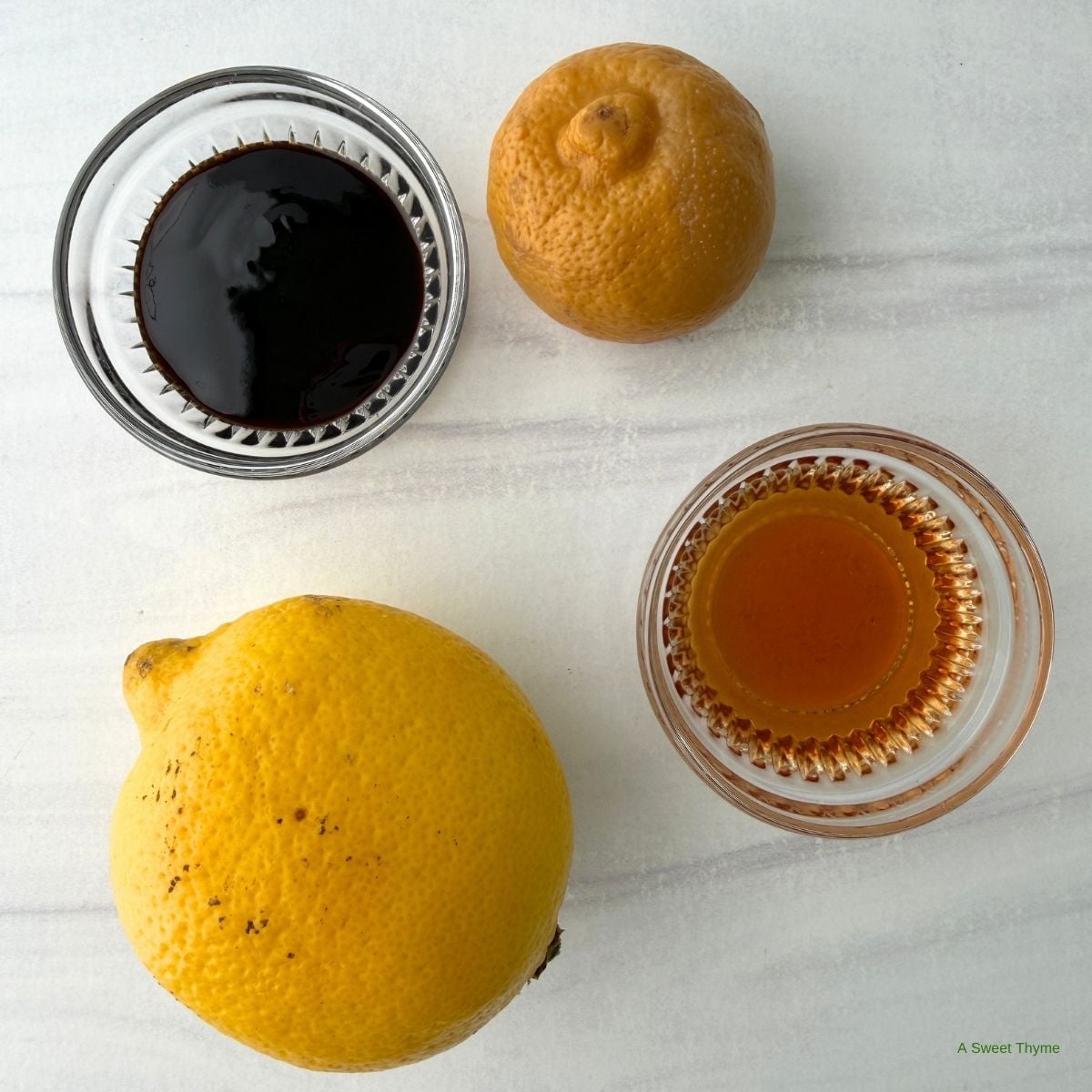 A fresh lemon, a wrinkled dried lemon, a small glass of dark liquid, and a small glass of light brown liquid arranged on a light surface—these essential ingredients are perfect for anyone exploring Mediterranean cooking or following a beginner’s guide to authentic Mediterranean recipes.