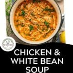 A pot of comforting Chicken and White Bean Soup with kale, featuring tender shredded chicken, is garnished with parsley and sits beside a bowl of chopped herbs. Text below reads: Chicken & White Bean Soup with Kale. Download Now.