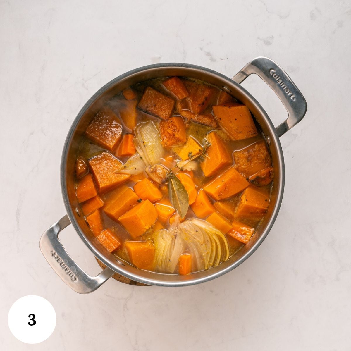A stainless steel pot filled with broth, chunks of roasted butternut squash, and halved onions for a warm spice soup.