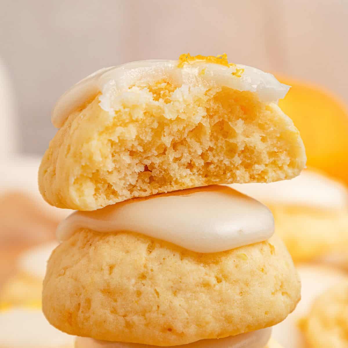 Two glazed lemon ricotta cookies stacked, with the top cookie broken in half to show the crumb.