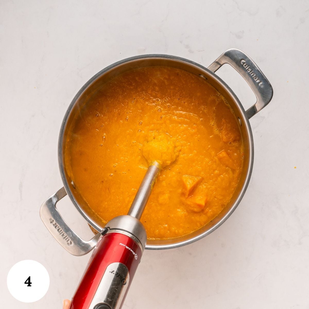 An immersion blender pureeing creamy carrot and butternut squash soup in a stainless steel pot.