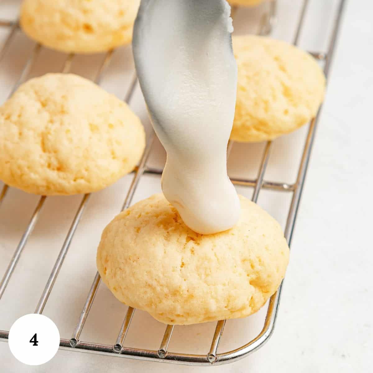 A spoon drizzles white icing onto a round lemon ricotta cookie sitting on a wire cooling rack.