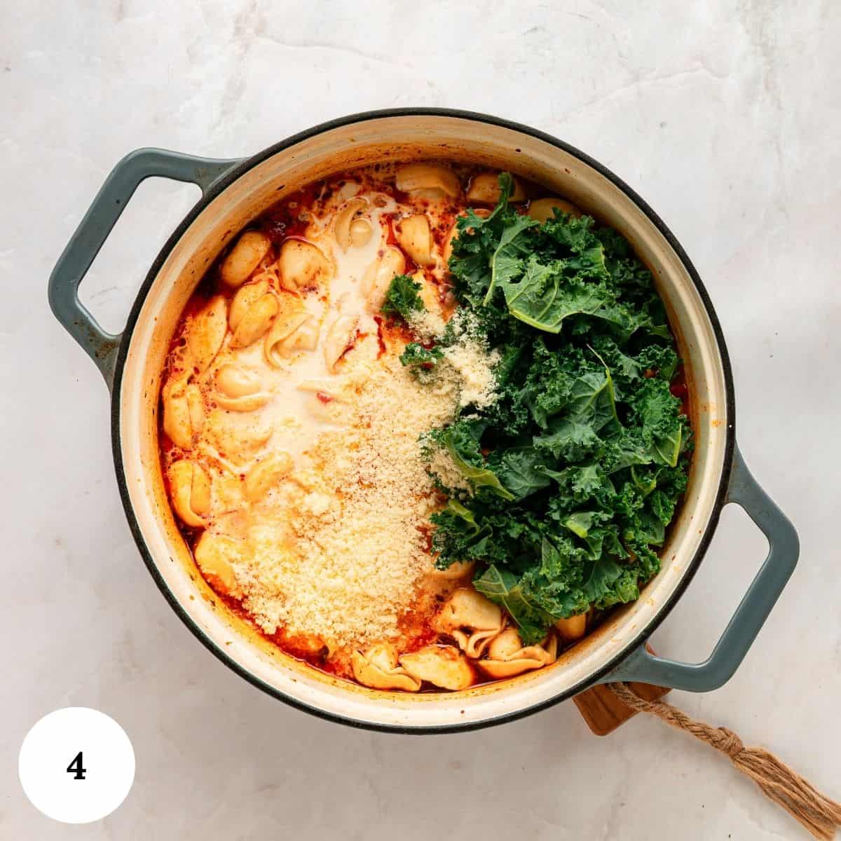 A pot of Tuscan tortellini soup in a creamy tomato sauce, topped with grated cheese and a pile of fresh kale.