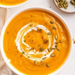 A bowl of butternut squash soup swirled with cream, garnished with pumpkin seeds and herbs.