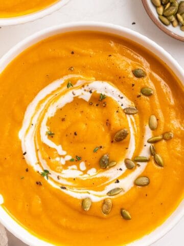 A bowl of butternut squash soup swirled with cream, garnished with pumpkin seeds and herbs.