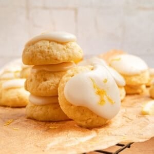 Stack of lemon ricotta cookies with a lemon glaze and zest on parchment paper.