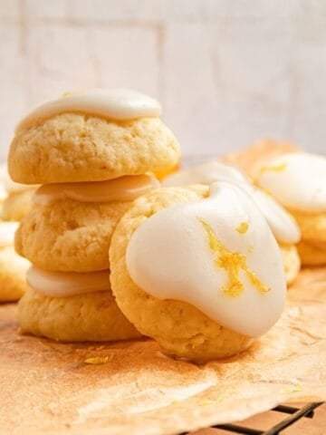 Stack of lemon ricotta cookies with a lemon glaze and zest on parchment paper.